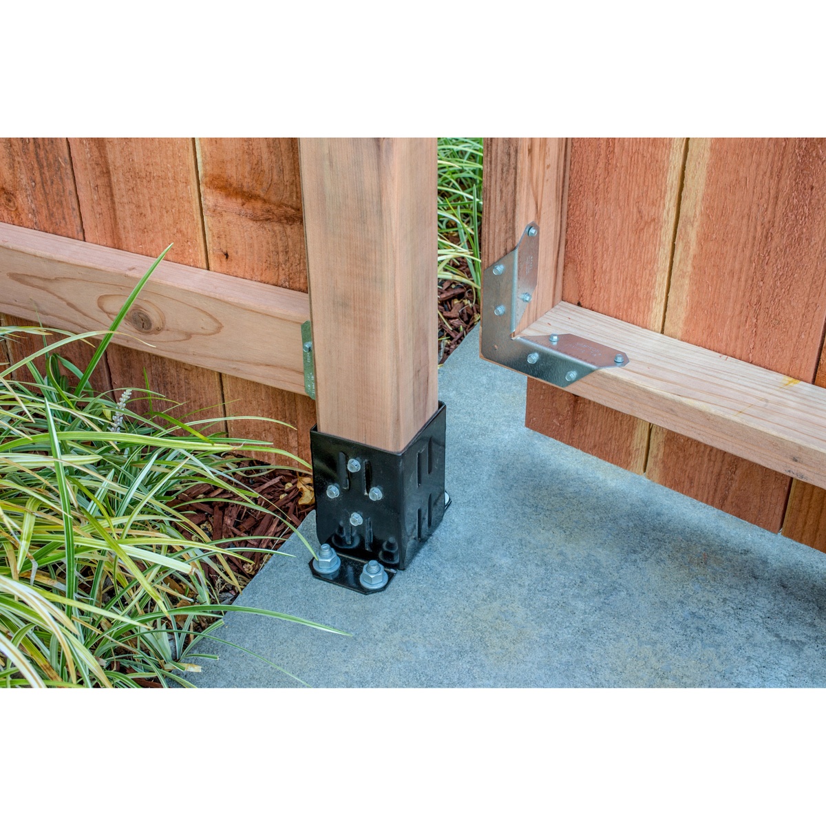 Simpson Strong-Tie FPBB44 E-Z Base post base securing a 4x4 wood gate post to an existing concrete path in a fence installation