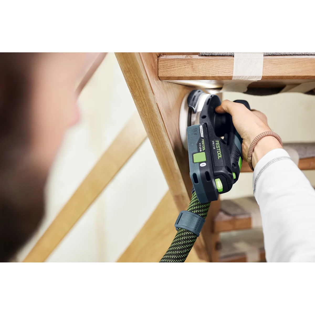 Festool edge sanding accessory installed on an ETSC 2 125 cordless orbital sander working under a wooden chair seat in a tight sanding area
