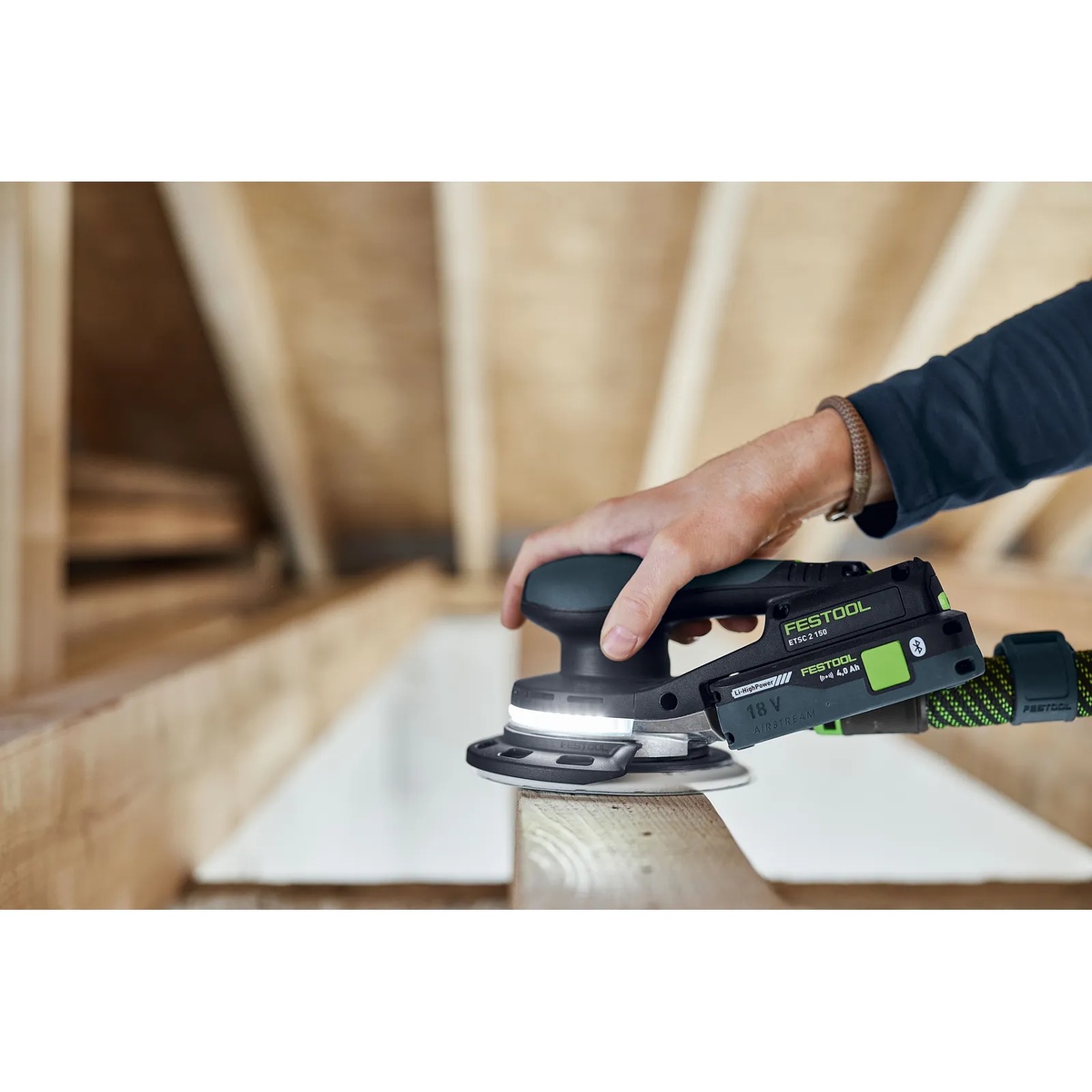 Festool ETSC 2 150 cordless orbital sander with protector sanding along the edge of a wood board on a framing-style work surface
