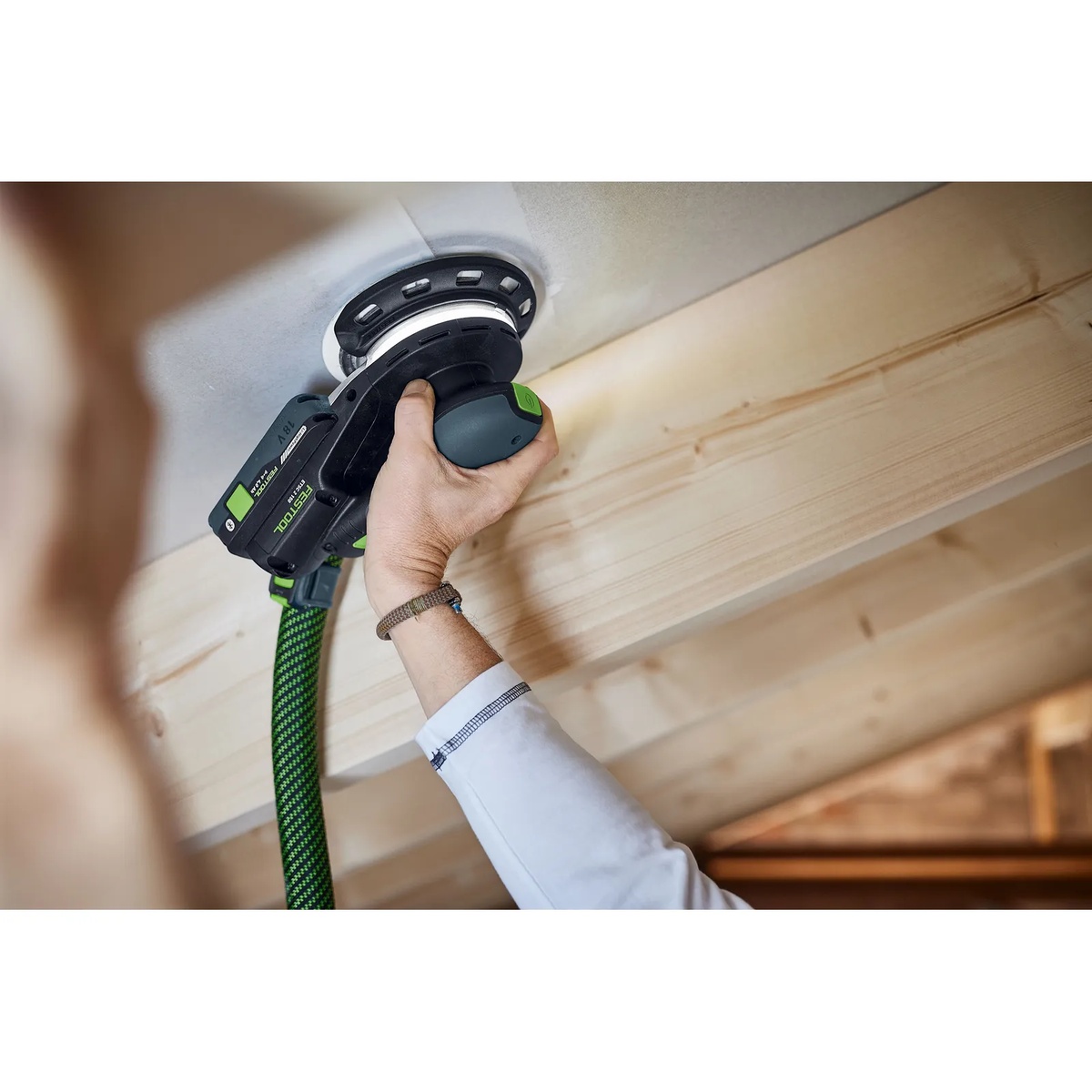 Festool ETSC 2 150 sander with protector sanding overhead on a finished surface near a wood beam during interior work