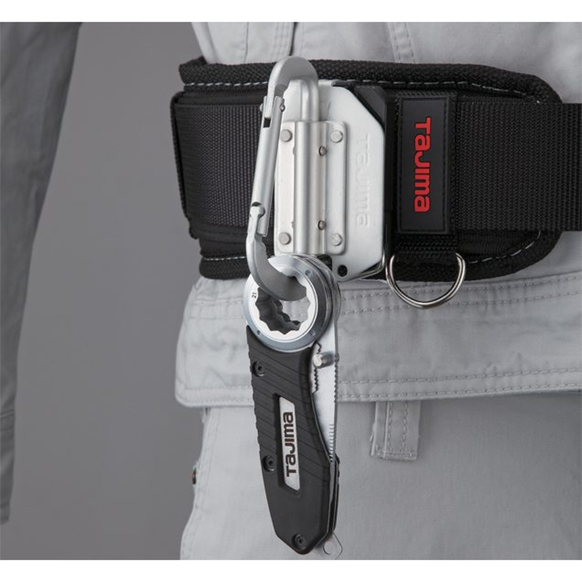Tajima VARIX Folding Compact Knife clipped to a tool belt on a jobsite for quick access between cuts and fastening tasks