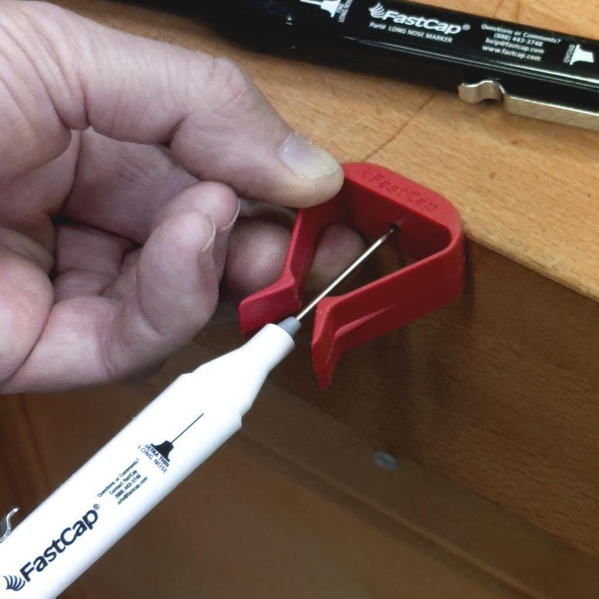 FastCap Long Nose Marker Thin Black marking through a red hardware clip on a wood cabinet surface during detailed installation work