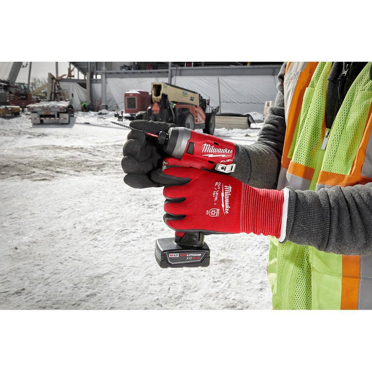 Milwaukee 48-22-8910 insulated winter work gloves being used to hold a cordless impact driver on a snowy construction jobsite