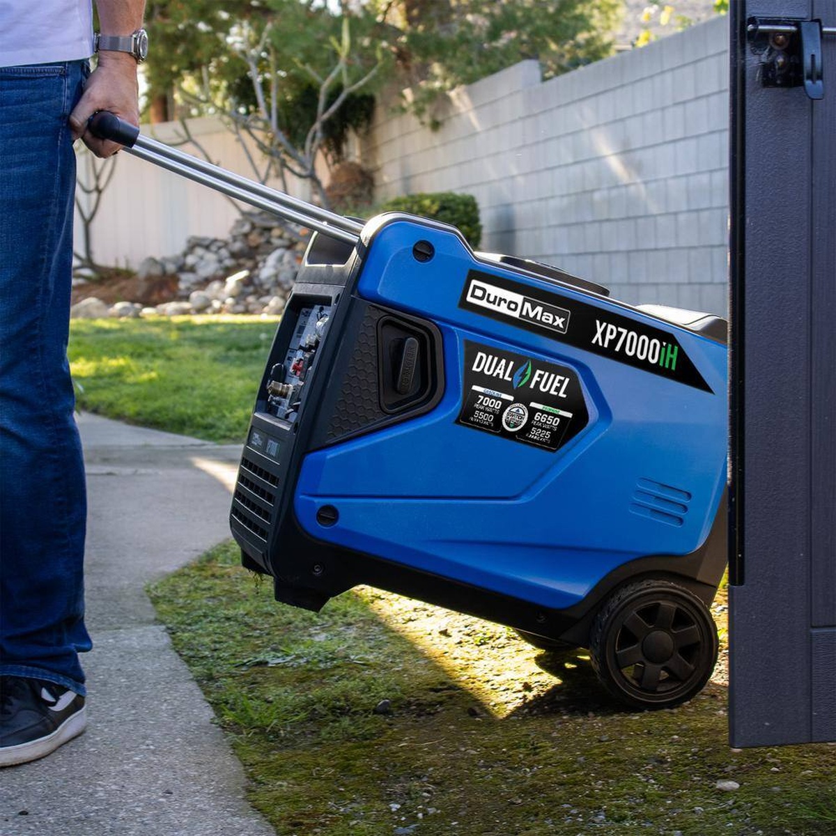 DuroMax XP7000iH Dual Fuel Portable Digital Inverter Generator being rolled into position outside a house for backup power use