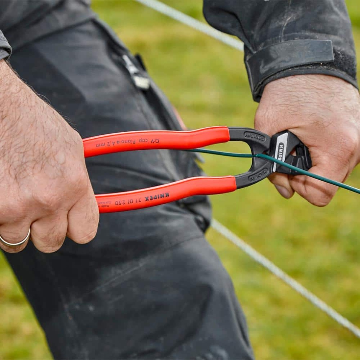 KNIPEX compact bolt cutter gripping and pulling wire during fence wire installation in an outdoor work setting