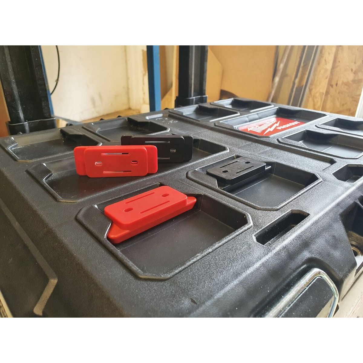 StealthMounts Milwaukee PACKOUT Feet Red 8-Pack installed on a Milwaukee PACKOUT surface in a workshop setup for custom accessory mounting