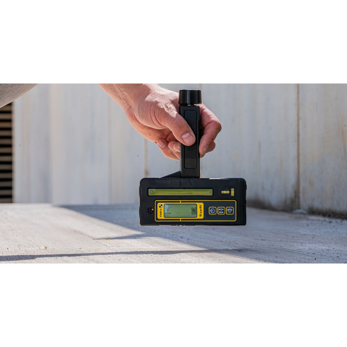 Stabila RL 230 RG Line Receiver used by hand to locate a laser reference line on a concrete surface during layout work