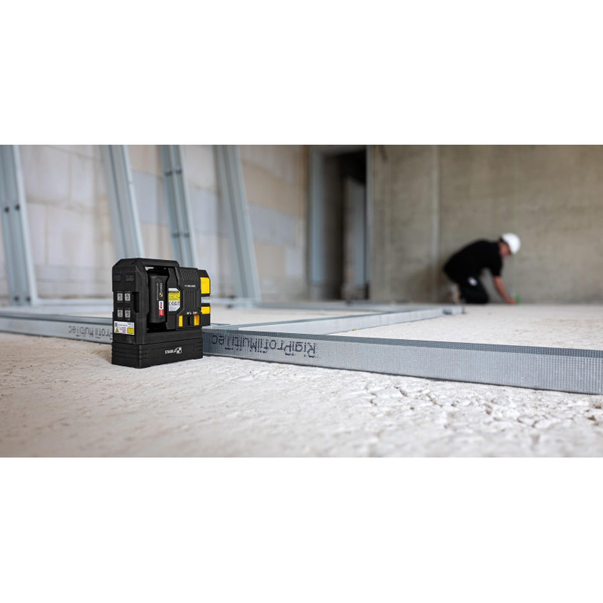 Stabila Cross-line plumb laser LAX 500 G, 12 V system used for interior framing layout on a construction floor beside metal track in a commercial jobsite setting