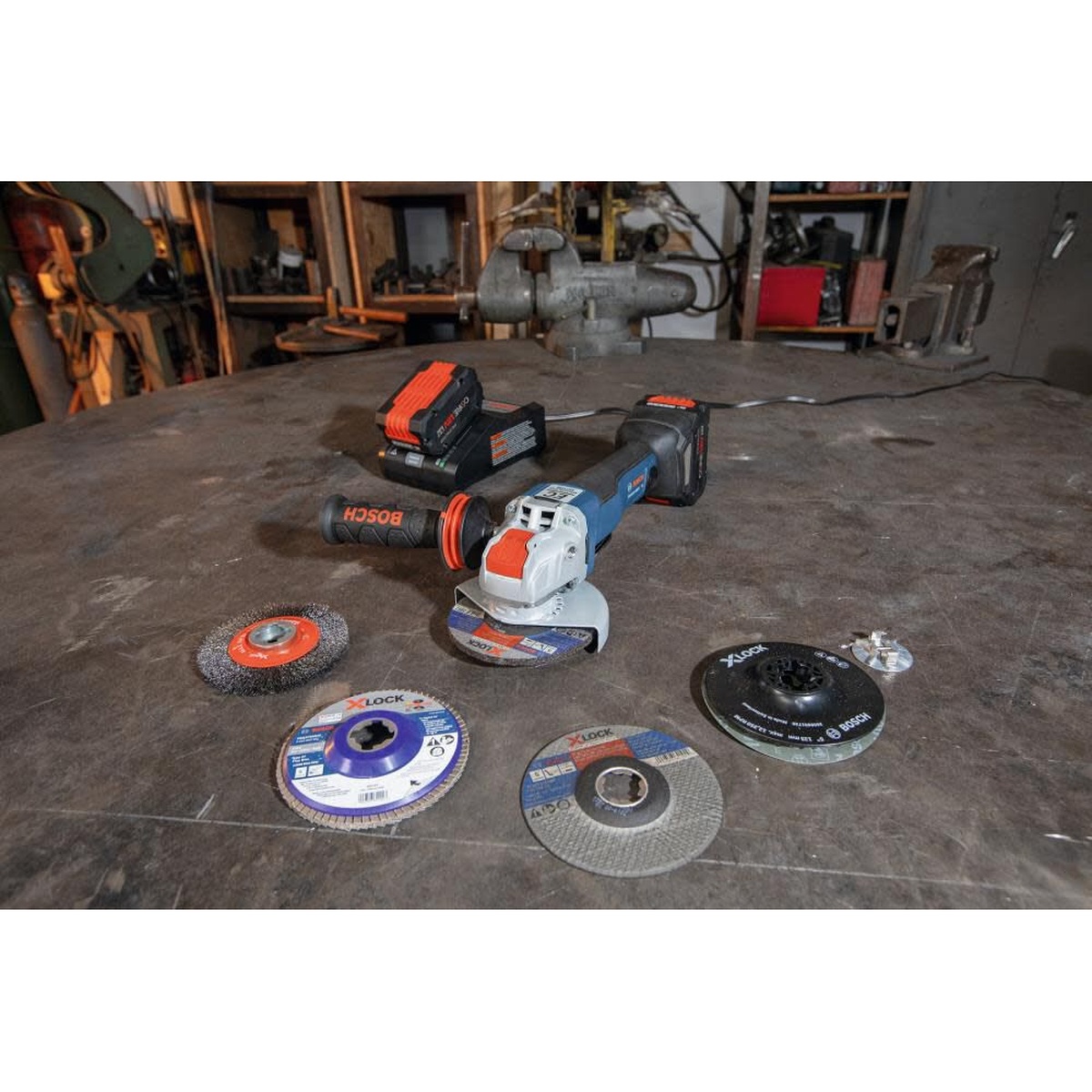 Bosch X LOCK Arbor Type 29 40 Grit Flap Disc 4 1/2in displayed with X-LOCK grinder accessories on a metal fabrication workbench in a shop