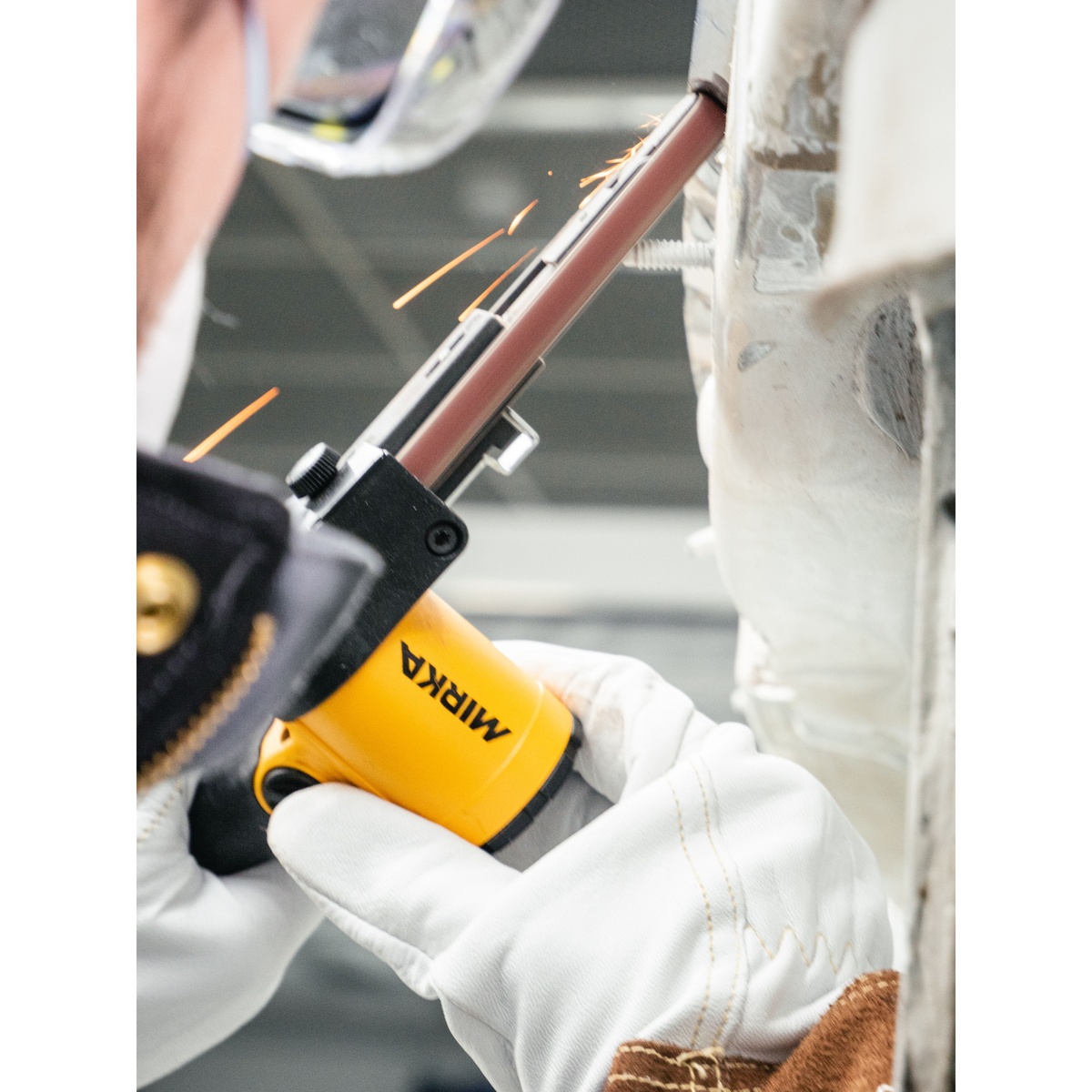 Mirka PBS-13457 Pneumatic Belt Sander sanding a weld area on sheet metal with sparks during automotive repair