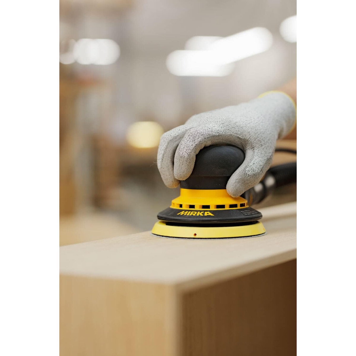 Mirka DEROS 550CV random orbital sander sanding a wood panel in a workshop during finish prep