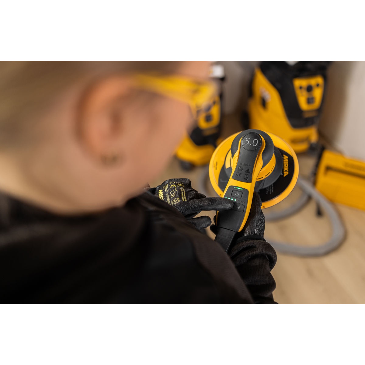 Mirka DEROS II 750X random orbital sander in use on a large flat work surface in a shop setting, showing top controls during surface sanding