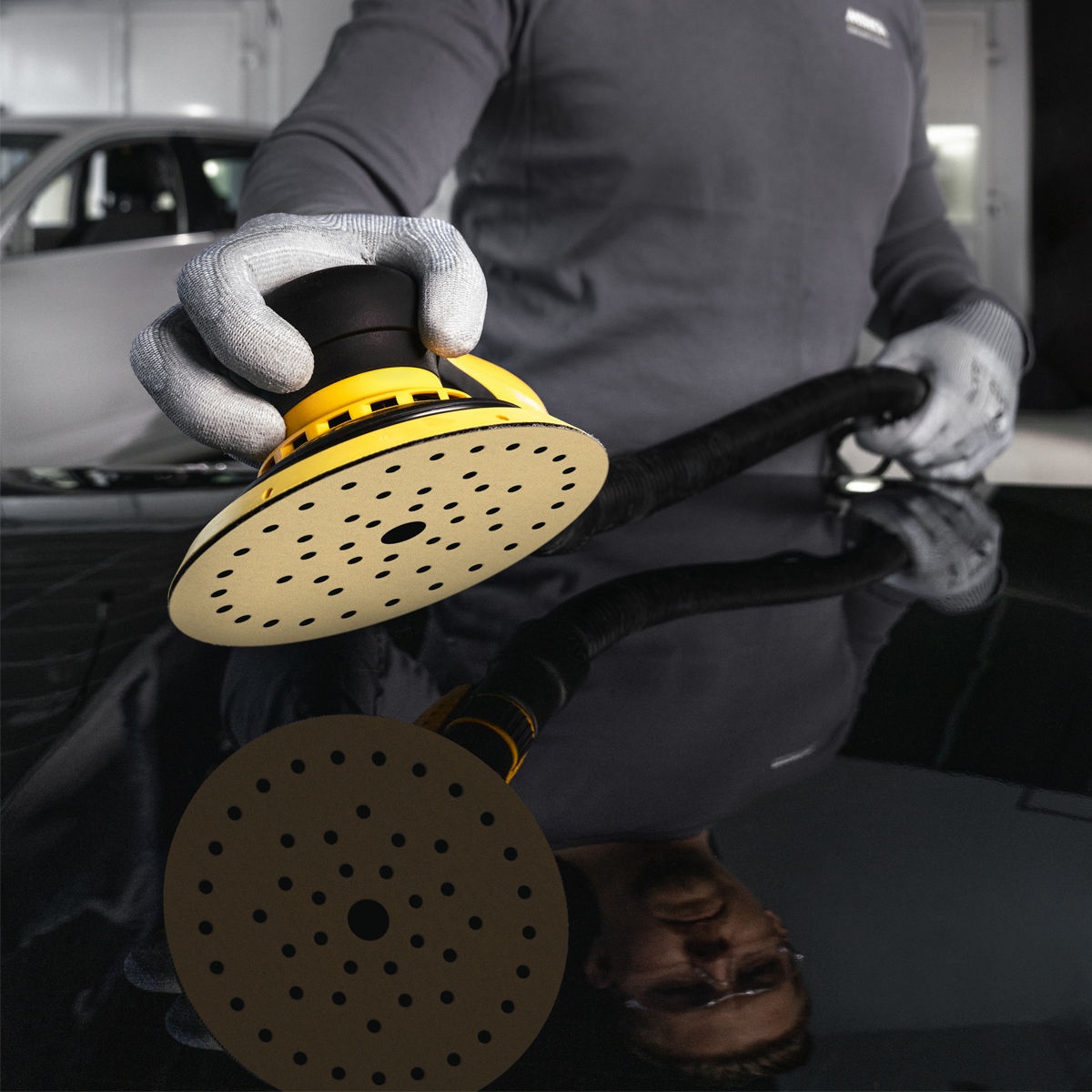 Mirka Gold 6 inch Grip Multifit sanding disc mounted on a random orbit sander for automotive paint sanding on a vehicle panel in a shop