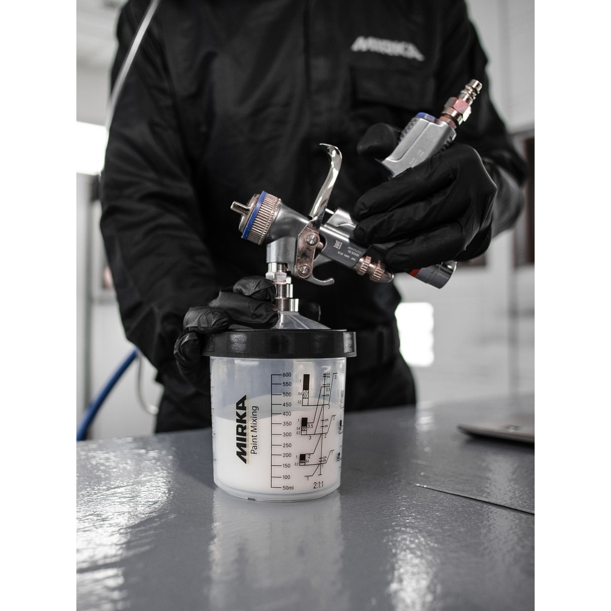 Mirka Paint Cup System with 190 micron Filter Lids attached to a spray gun during paint mixing and refinishing setup on a workshop bench