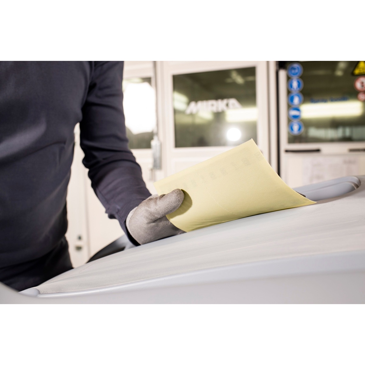 Mirka NOVASTAR FLEX 5.1 x 6.7 Grip Perf hand sanding sheet bending over a contoured automotive panel during dry sanding work
