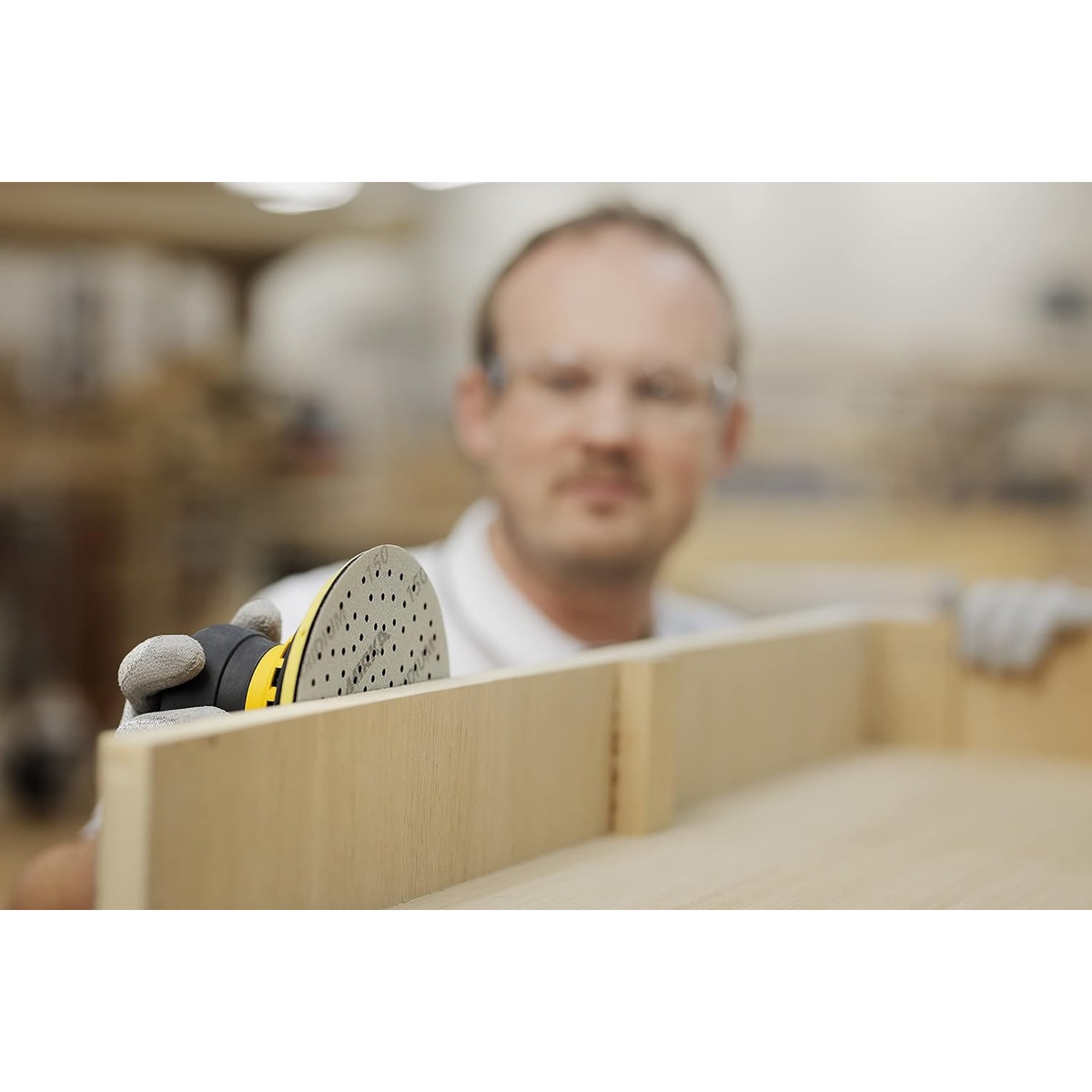 Mirka Iridium Premium Sandpaper Ø 6-Inch Hook & Loop, Grit 40 installed on a random orbital sander for sanding a wood panel in a workshop setting