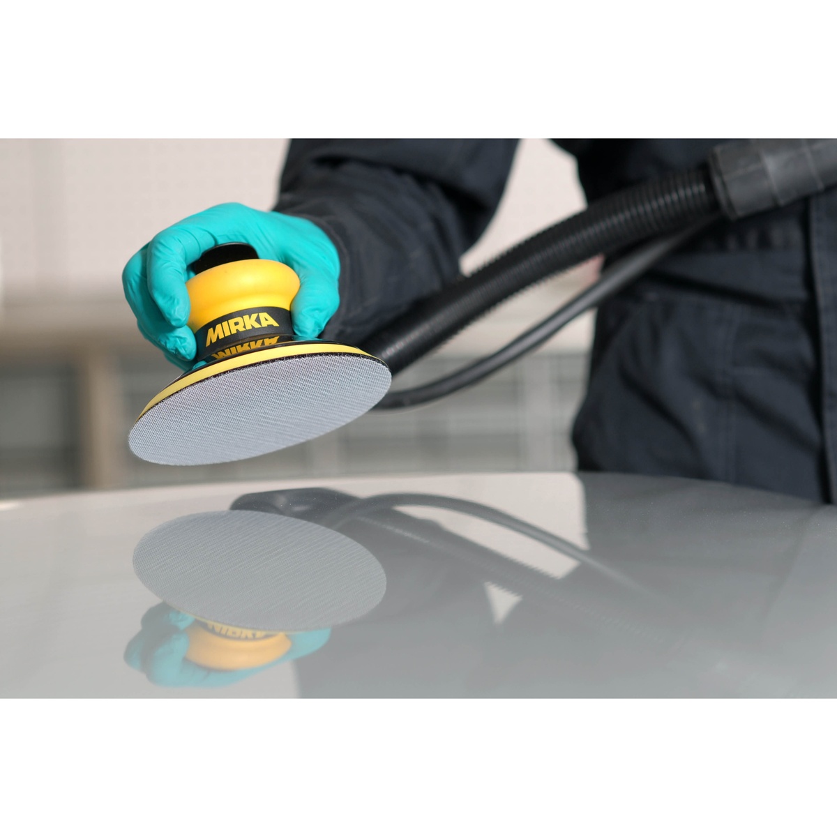 Mirka AE24105012 Autonet Grip Disc installed on a sanding tool during automotive refinishing on a painted panel with dust extraction connected