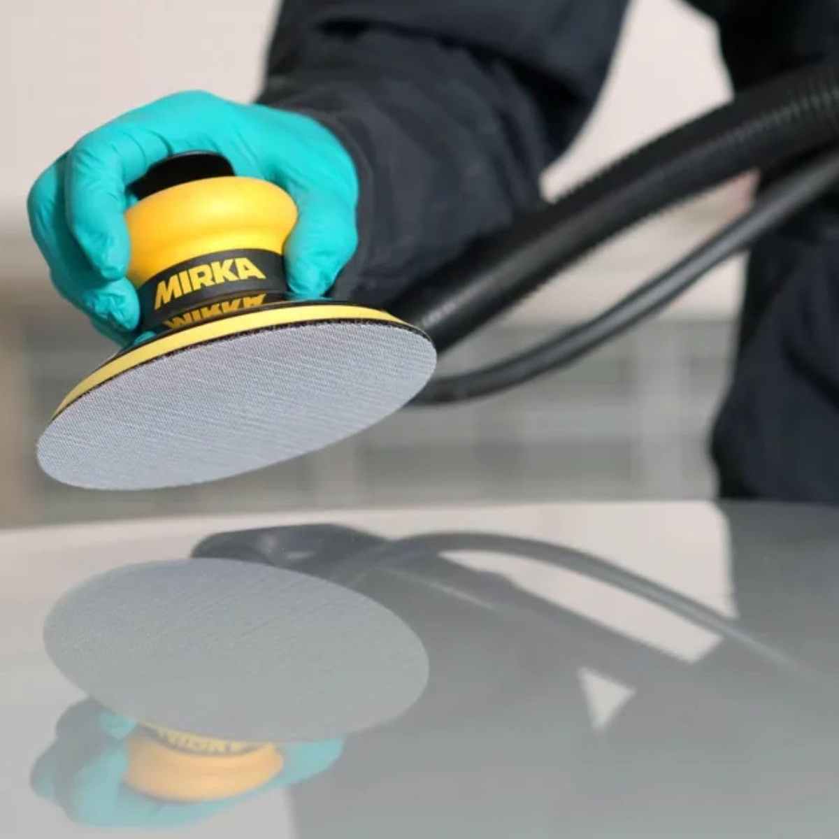 Mirka AE23205025 Autonet 240 Mesh Grip Sanding Discs installed on a 5 inch random orbital sander during automotive refinishing on a smooth painted panel