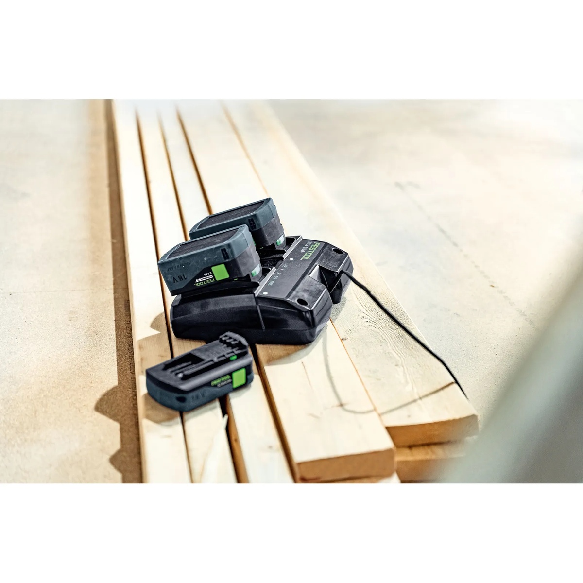 Festool SYS 18V 4xHP5,0/TCL6DUO batteries charging on the dual charger over wood boards in a workshop setting