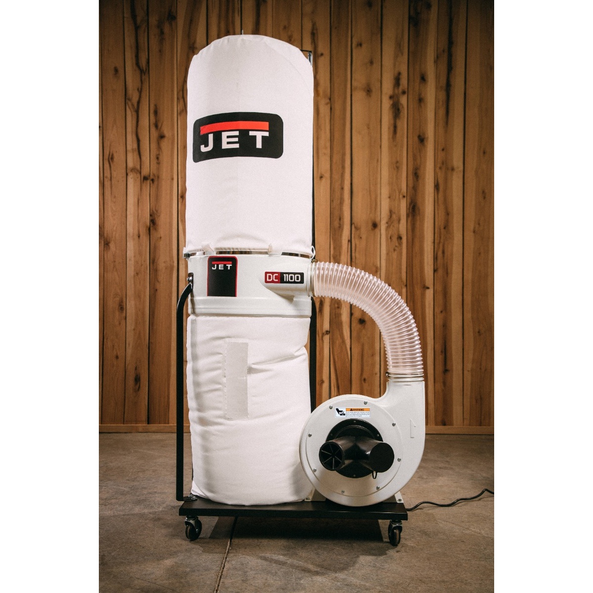 JET DC-1100VX-5M Dust Collector standing in a woodshop setup, showing the bag filter, lower collection bag, and hose routing for woodworking dust collection