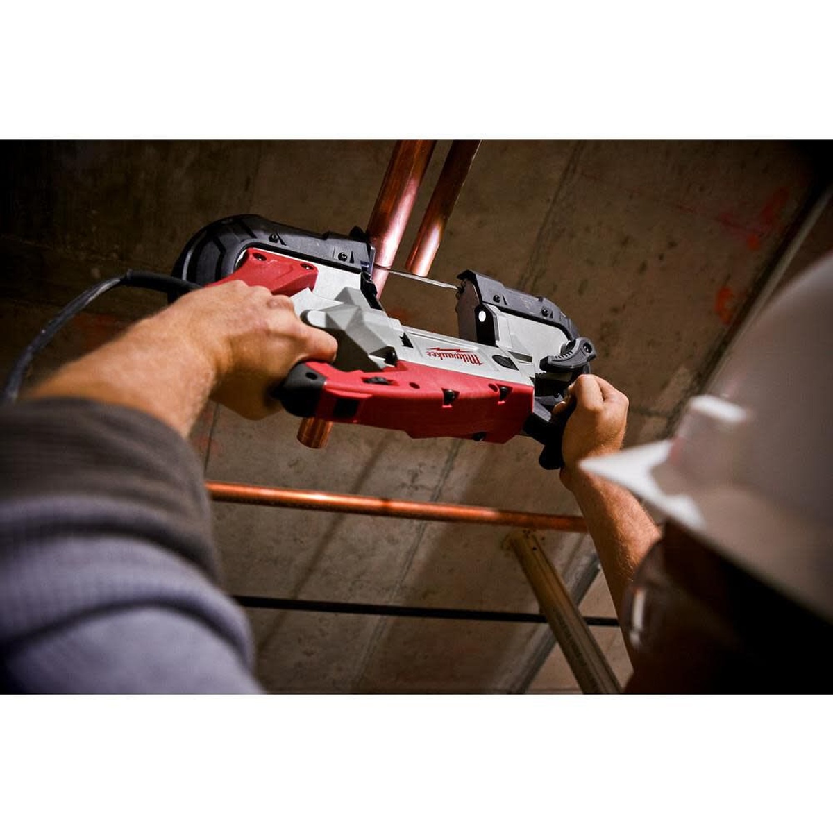 Milwaukee Deep Cut Variable Speed Band Saw Kit cutting overhead copper pipe in a commercial mechanical space