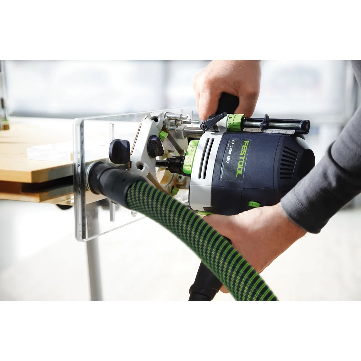 Festool OF-FH 2200 Routing Aid guiding a Festool router along the edge of a wood panel during groove routing with dust extraction connected in a workshop setting