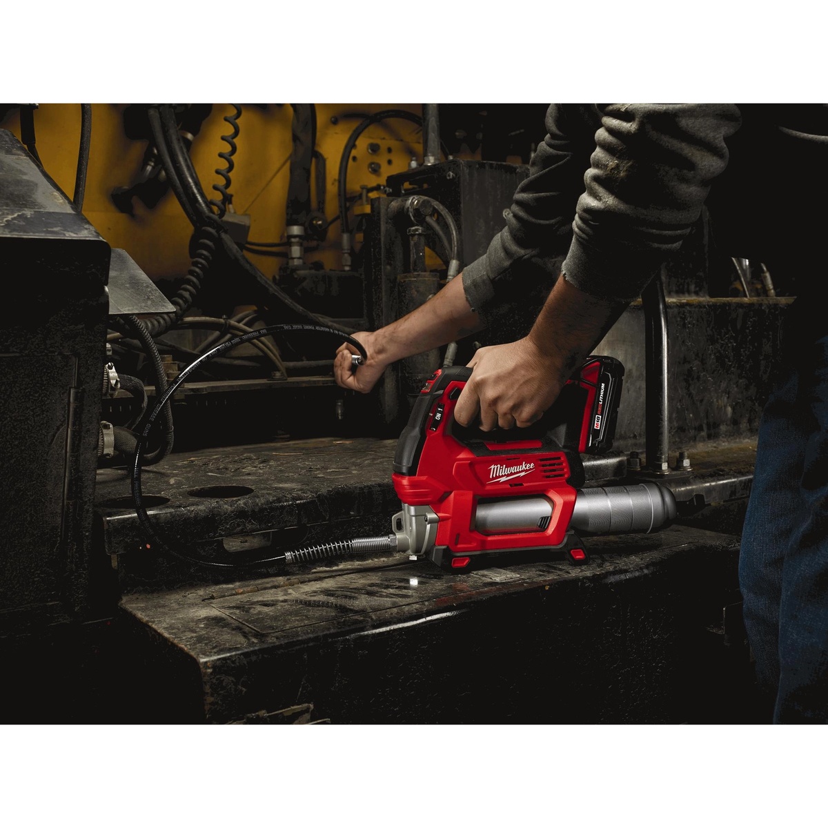 Milwaukee 2646-21CT M18 Cordless 2-Speed Grease Gun Kit being used on heavy equipment with the 48 inch hose reaching a grease fitting in a dark service area