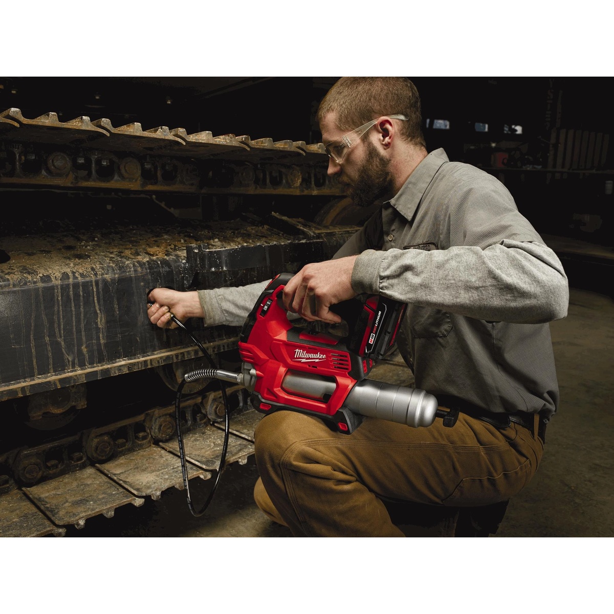 Technician using Milwaukee 2646-21CT M18 Cordless 2-Speed Grease Gun Kit on tracked equipment during maintenance service in a shop