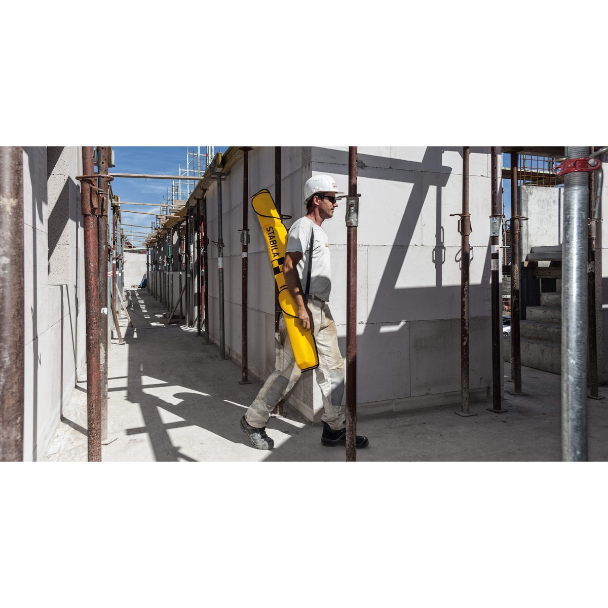 Stabila 30025 Nylon Carrying Case being carried through an active construction site with scaffolding for transporting spirit levels between work areas