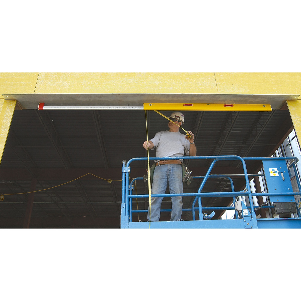Stabila 34610 6-to-10-foot Expandable Magnetic Plate Spirit Level extended across a large framed opening while a worker measures height from a lift on a commercial jobsite