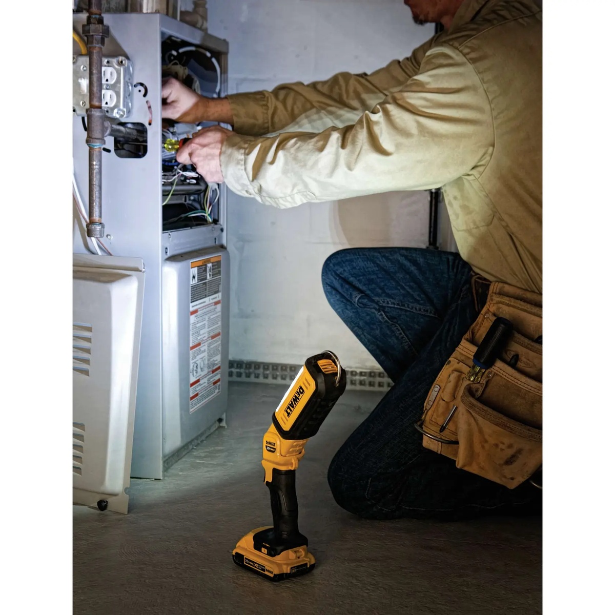 DEWALT DCL050 20V MAX LED Hand Held Area Light illuminating an HVAC service area while a technician works inside equipment in a dim mechanical room