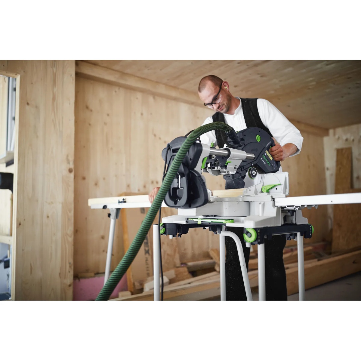 Festool 497351 UG-Kapex Wheeled Stand supporting a Festool KAPEX miter saw while cutting trim material inside a wood-framed interior jobsite