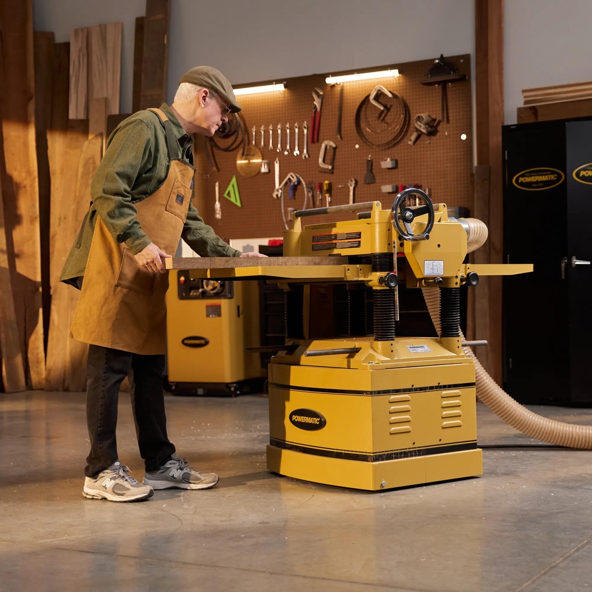 Powermatic 209HH 20-Inch Planer surfacing a wide hardwood board in a woodworking shop with dust collection connected during thickness planing