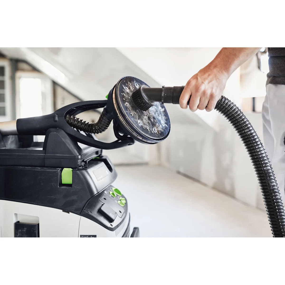 Festool suction brush attached to a dust extractor hose and used to clean a sanding pad in a workshop setting