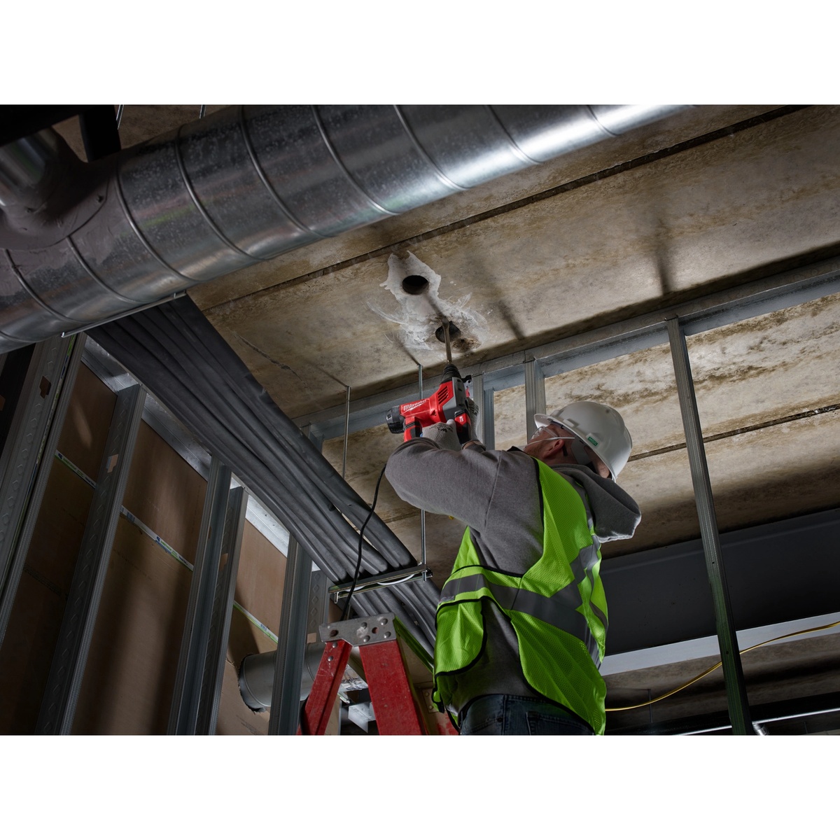Milwaukee 1-1/8 In. SDS Plus Rotary Hammer Kit drilling overhead into a concrete ceiling on a commercial jobsite framing area