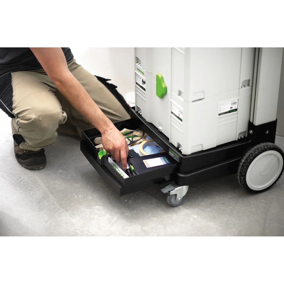 Festool 498660 Sys-Roll Systainer Cart drawer pulled open on a jobsite floor with tape, accessories, and small parts stored under stacked Systainers