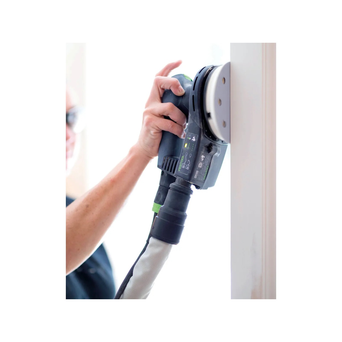 Festool ETS EC 125/3 EQ-Plus Random Orbital Sander sanding a vertical painted wood surface during finish prep with dust hose attached in an indoor jobsite setting