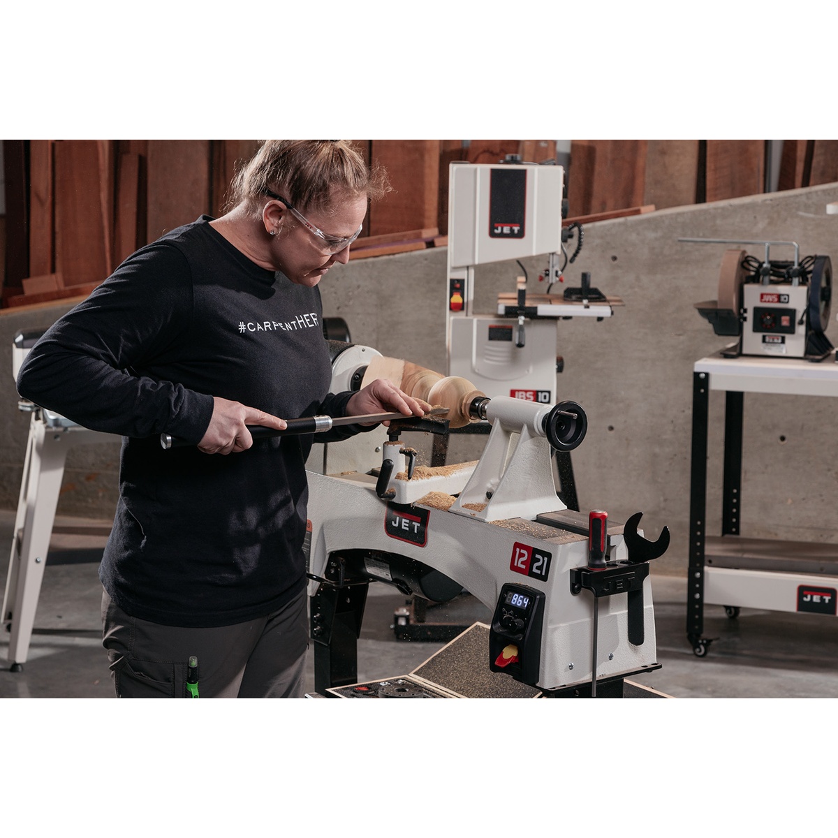 Jet 719200 JWL-1221VS 12 x 21 variable speed wood lathe turning a wood workpiece in a shop with the operator using a turning tool at the rest