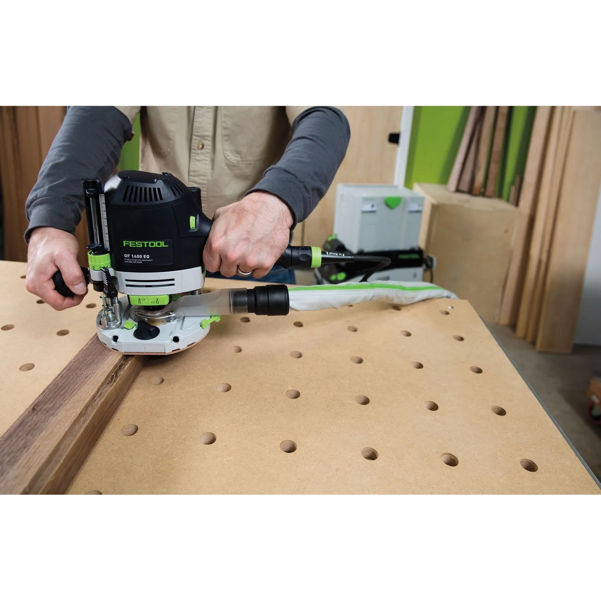 Festool OF 1400 EQ-F-Plus Plunge Router routing a hardwood board on a perforated workbench with dust extraction connected in a woodworking shop