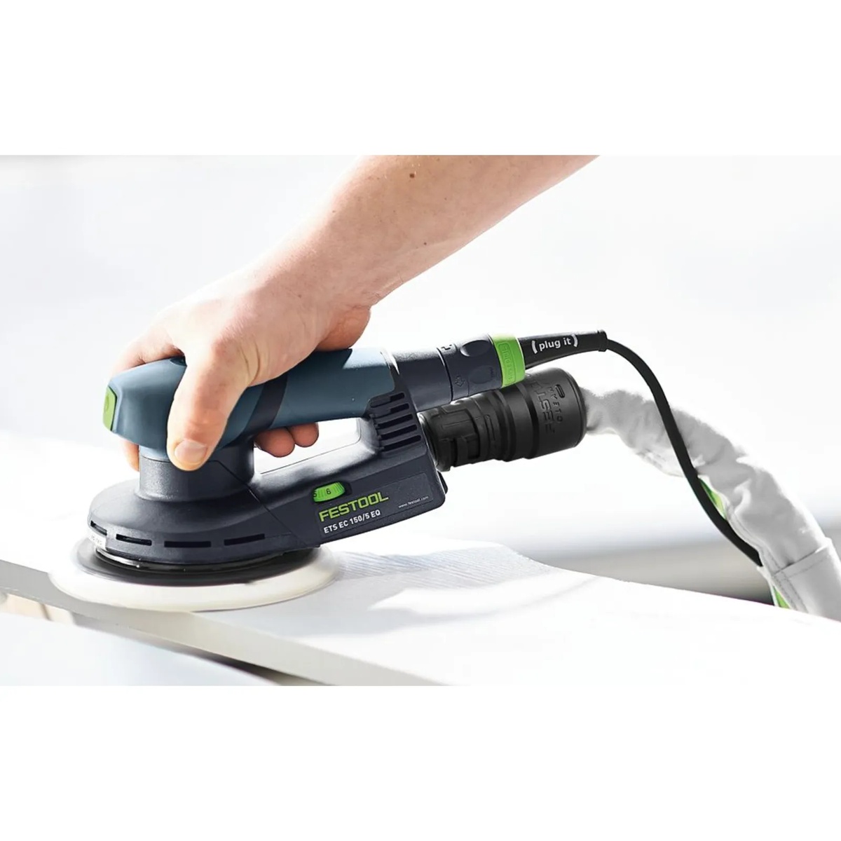 Festool D 32/22x10m-AS-GQ/CT USA suction hose connected to a Festool sander while sanding a panel in a workshop, showing the sleeve-covered hose and integrated Plug It cord in use
