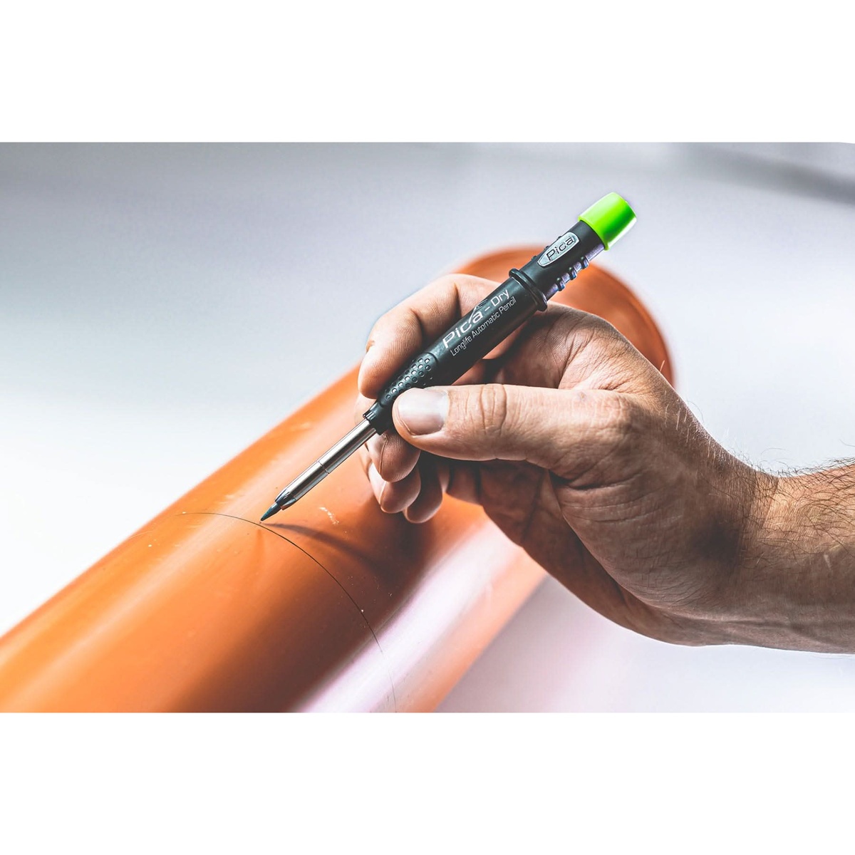 Pica Dry 3030 Pencil + 4030 Black Lead Refill marking a smooth orange pipe during plumbing or HVAC layout work
