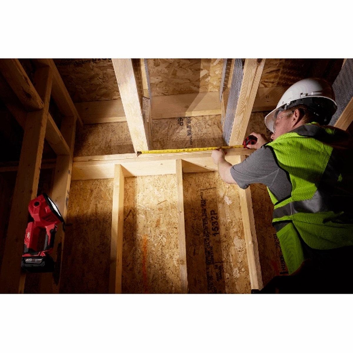 Milwaukee 2354-20 M18 Search Light mounted in a framed wall cavity lighting a construction workspace for measuring
