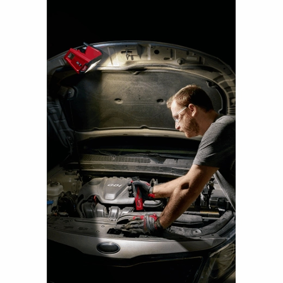 Milwaukee 2364-20 M12 ROVER Mounting Flood Light attached under a vehicle hood to light an engine bay during automotive repair
