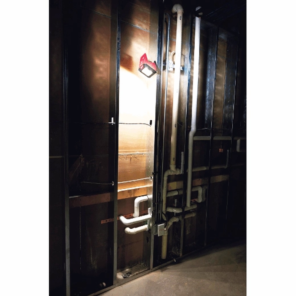 Milwaukee 2364-20 M12 ROVER Mounting Flood Light illuminating plumbing and framing inside a dark wall cavity during interior service work