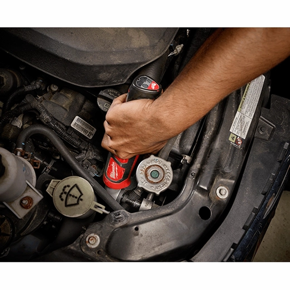 Milwaukee 2467-20 M12 1/4 inch Hex Right Angle Impact Driver being used in an automotive engine bay to reach a hard-to-access fastener during repair work