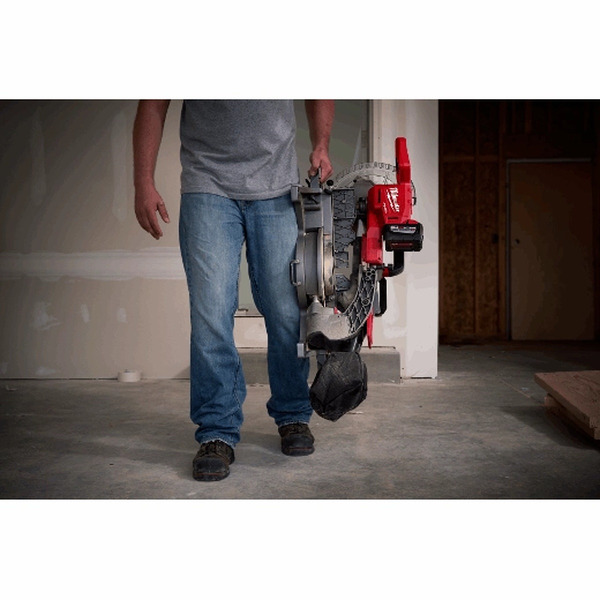 Milwaukee M18 FUEL dual bevel sliding compound miter saw being carried by a contractor across an indoor jobsite