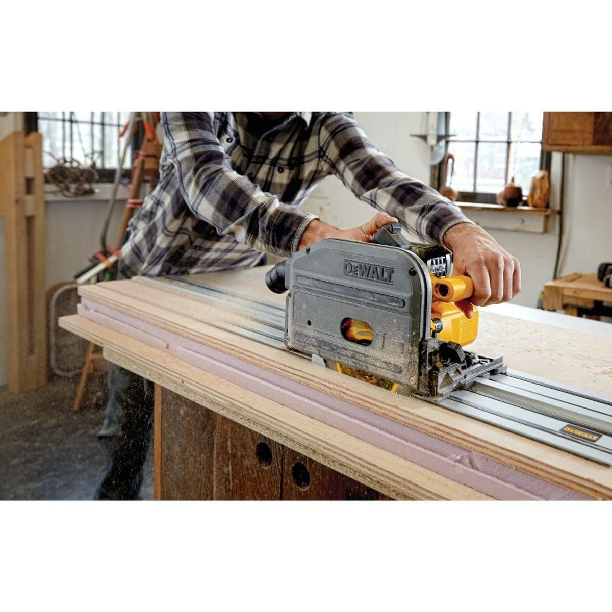DEWALT DCS520B 60V MAX 6-1/2 in. Cordless Track Saw making a long guided rip cut through plywood on a workbench in a woodworking shop