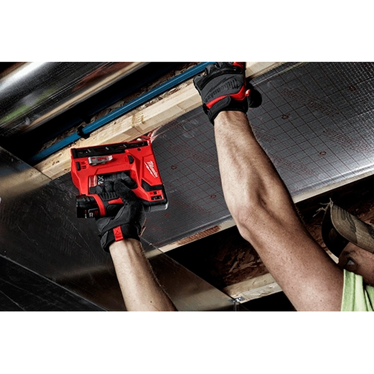 Milwaukee M12 3/8 in. Crown Stapler being used overhead on jobsite material installation between framing members