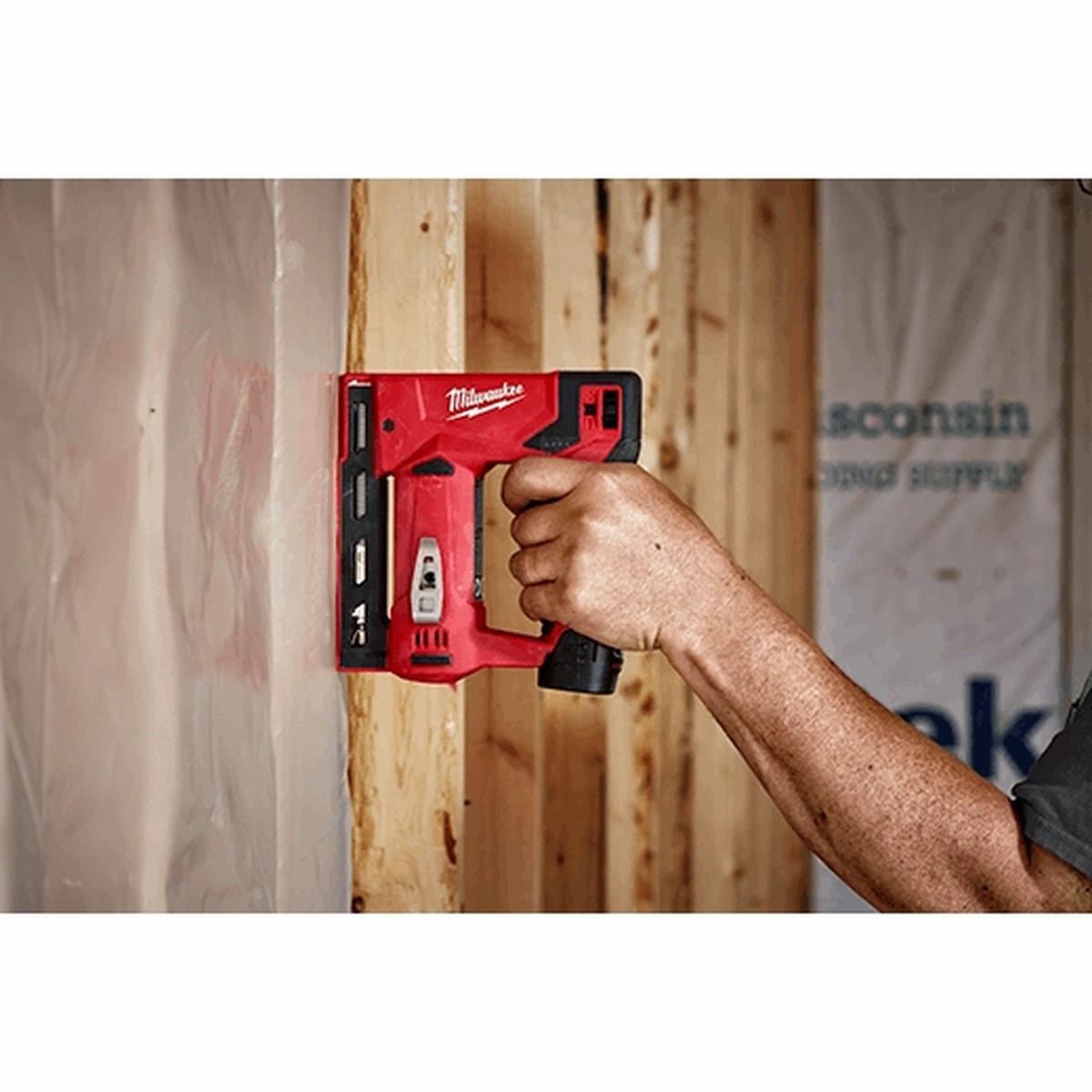 Milwaukee M12 3/8 in. Crown Stapler fastening material inside a framed wall bay during interior construction work
