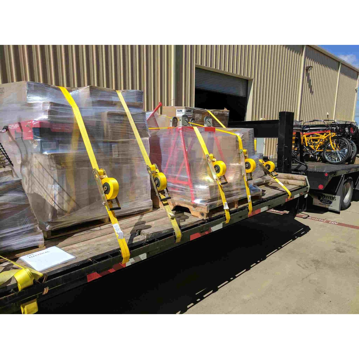 Quickloader QL100001 10000lb 27ft Ratchet Strap, 1-Pack securing wrapped pallet loads on a flatbed trailer at an industrial loading area
